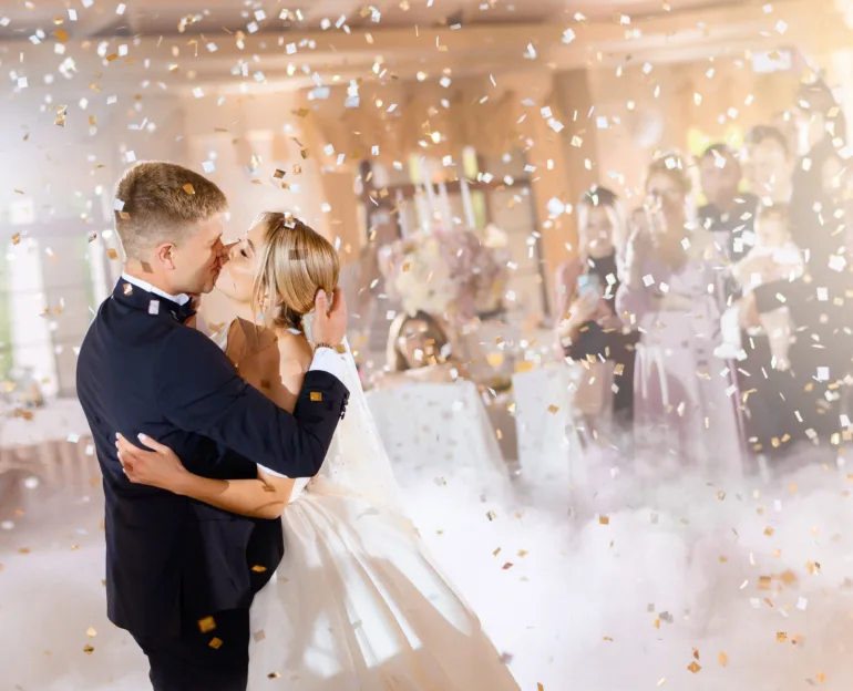 Posrtrait of tenderness couple, bride with groom kissing while falling confetti and enjoying celebration of wedding day, wearing in beautiful dress and suit.